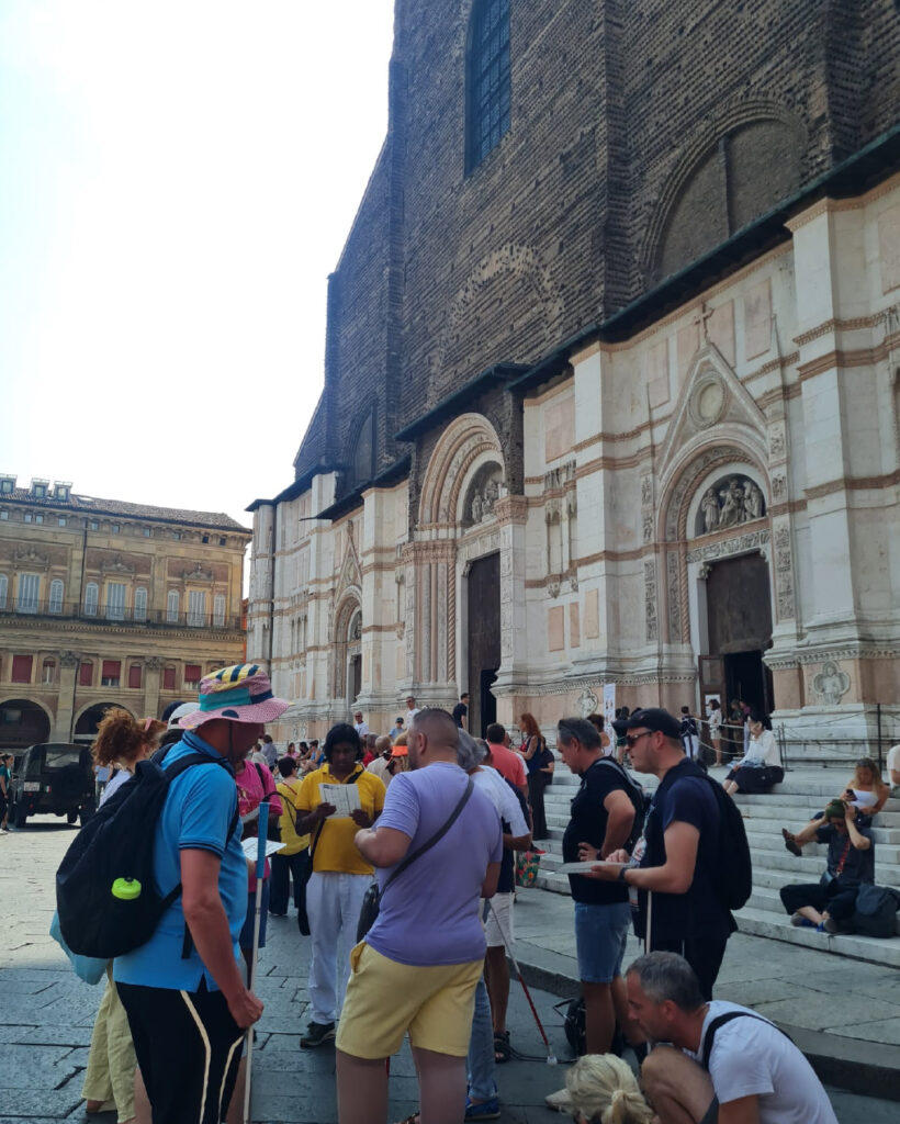 Il gruppo numeroso è davanti alla Basilica di San Petronio, alcune persone stanno esplorando una mappa tattile.