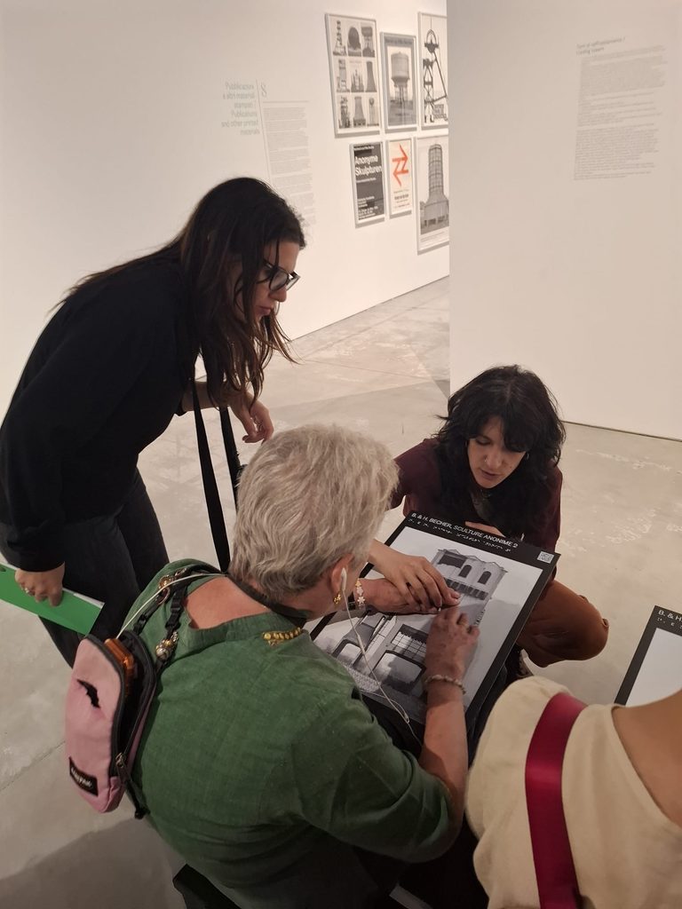 Due mediatrici illustrano un pannello tattile a una persona cieca