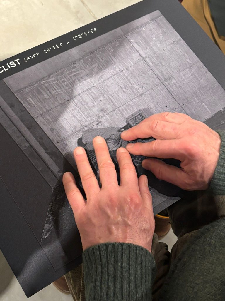 Due mani toccano il pannello tattile con la foto 'Cyclist' di Jeff Wall
